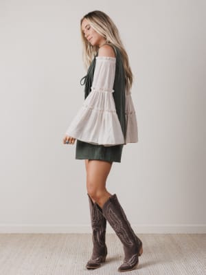 Woman wearing a white blouse, green skirt, and brown boots against a plain background