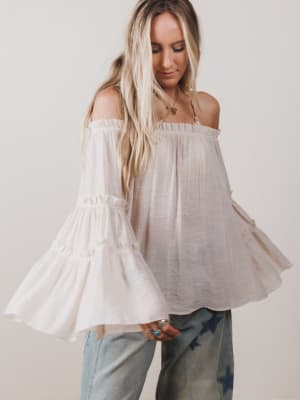 Woman wearing a white off-shoulder top with long sleeves against a plain background