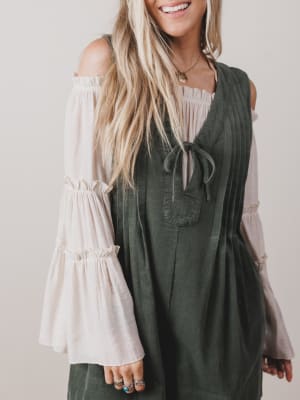 Woman wearing a green dress over a white blouse with long sleeves against a plain background