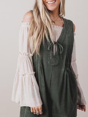 Woman wearing a green dress over a white blouse with long sleeves against a plain background