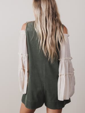 Person wearing a green romper with a white blouse underneath on a plain background