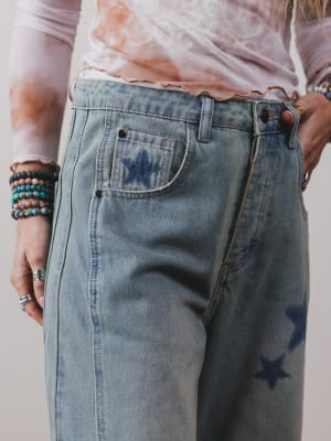 Person wearing light blue jeans with star designs, holding a phone.