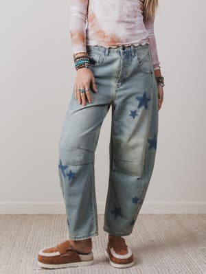 Person wearing tie-dye shirt and jeans with star patterns, standing against a plain background.