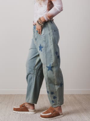Person wearing light blue jeans with star patterns and brown shoes on a neutral background
