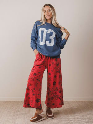 Woman wearing a blue sweatshirt with the number 03 and red patterned pants against a plain background