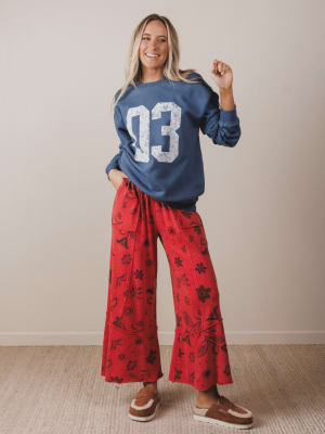 Woman wearing a blue sweatshirt with the number 03 and red patterned pants, standing against a plain background.