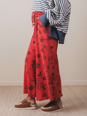 Person wearing a red floral skirt with a striped top and brown shoes on a neutral background
