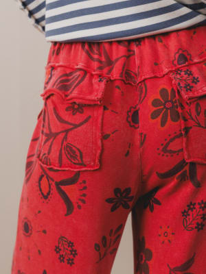 Red pants with black floral patterns worn over a striped shirt.