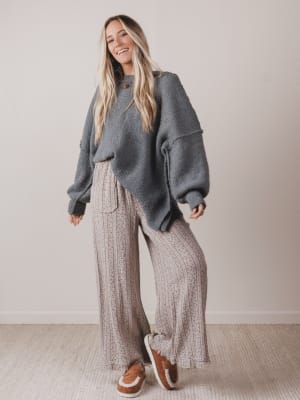 Woman wearing a gray sweater and patterned pants standing against a plain background