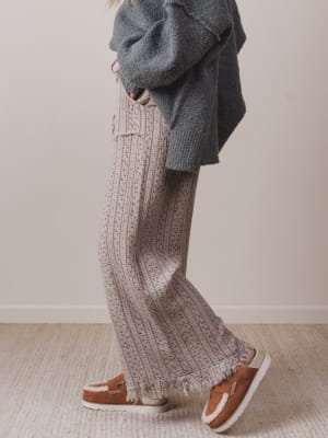Person wearing a gray sweater and patterned pants on a neutral background