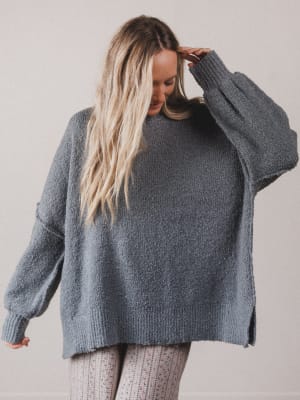 Woman wearing a gray oversized sweater against a plain background