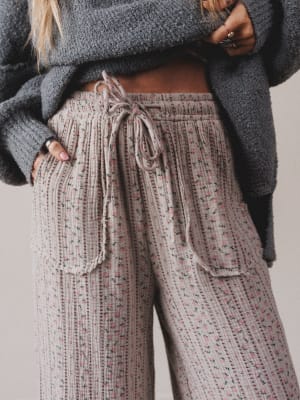 Person wearing a textured sweater and patterned pants with a neutral background