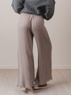Person wearing patterned pants and a gray sweater on a neutral background