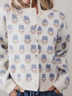 Person wearing a cream-colored cardigan with blue floral patterns on a plain background