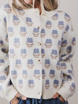Person wearing a cream-colored cardigan with blue floral patterns on a plain background