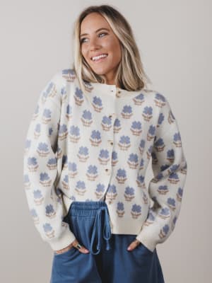 Woman wearing a patterned sweater and blue pants against a plain background