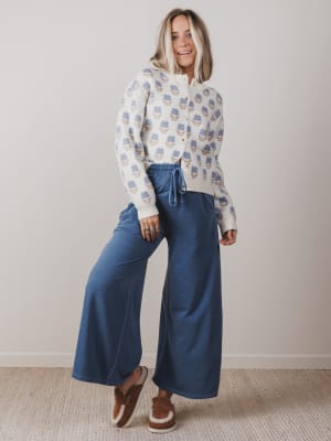 Woman wearing a patterned sweater and blue pants against a plain background