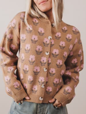 Person wearing a brown sweater with pink floral pattern against a neutral background