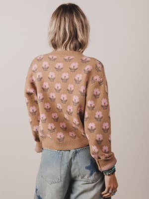 Person wearing a brown sweater with floral pattern and light blue jeans against a plain background