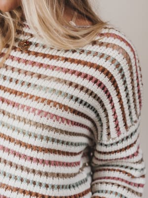 Close-up of a person wearing a multicolored striped sweater with a neutral background
