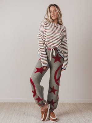 Woman wearing a striped sweater and star-patterned pants with brown shoes on a plain background