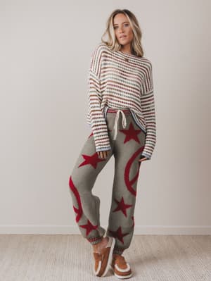 Woman wearing a striped sweater and star-patterned pants with brown shoes on a plain background
