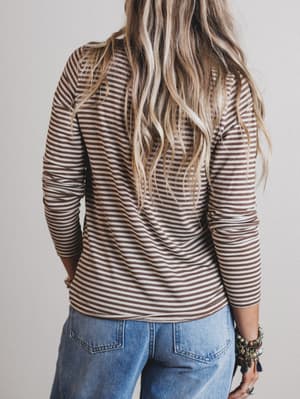 Person wearing a striped long-sleeve top and blue jeans with a neutral background