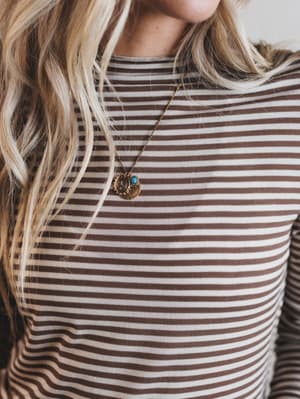 Person wearing a striped shirt with a necklace featuring a pendant.