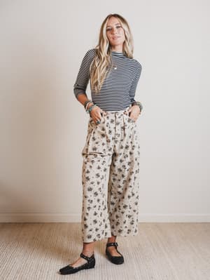 Woman wearing a striped long-sleeve top and floral pants against a plain background