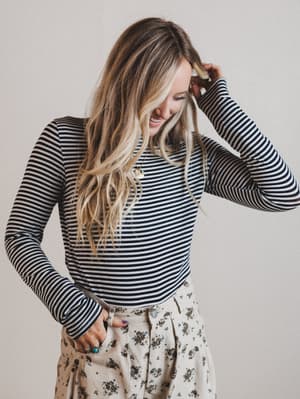 Woman wearing a striped long-sleeve top and floral pants against a plain background