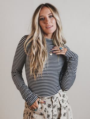 Woman wearing a striped long-sleeve top and floral pants against a plain background