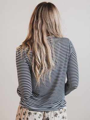 Back of a woman wearing a striped long-sleeve top and floral pants against a plain background