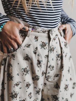 Person wearing a striped shirt and floral skirt with hands in pockets.