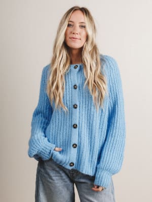 Woman wearing a blue knitted cardigan with black buttons on a plain background