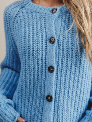 Close-up of a blue knitted cardigan with buttons on a neutral background