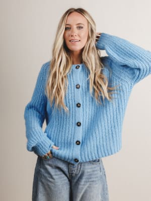 Woman wearing a blue knitted cardigan with black buttons on a plain background