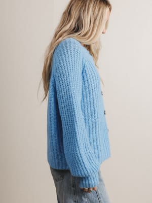 Side view of woman wearing a light blue chunky knit sweater against a beige background