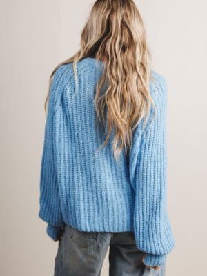 Back view of woman wearing a blue knitted sweater with a neutral background