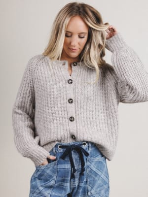 Woman wearing a gray chunky knit cardigan and plaid pants against a plain background