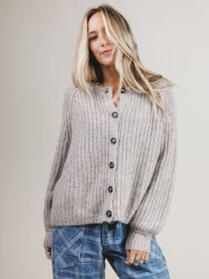 Woman wearing a gray chunky knit cardigan and plaid pants against a plain background