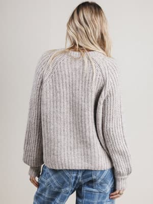 Back view of woman wearing a chunky knit sweater and plaid pants against a plain background