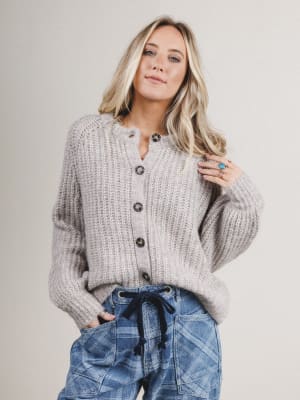Woman wearing a gray chunky knit cardigan and blue jeans against a plain background