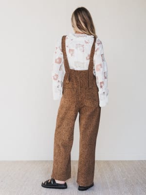 Person wearing brown patterned overalls and a white blouse with floral design.