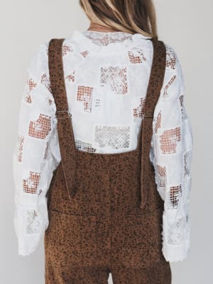 Person wearing a white lace top and brown overalls with a neutral background
