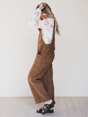 Person wearing a brown overalls and white lace top against a plain background