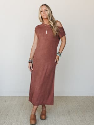 A rust knit midi dress worn with effortless off-shoulder styling, stacked boho bracelets, and tan clogs — the kind of outfit that looks like you tried the right amount.