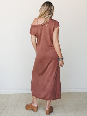 A knit midi dress in warm rust photographed from the back, styled with wood-soled clogs and a stack of mixed bracelets — the kind of effortless outfit that looks like you thought about it just enough.