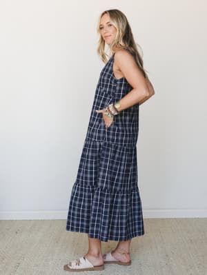 A navy plaid tiered maxi dress styled with white slide sandals and a stack of mixed bracelets — the kind of effortless, put-together look that works just as hard at a farmers market as it does at a casual dinner.