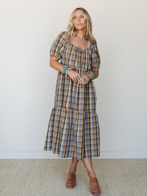 A plaid midi dress in warm earthy tones gets a boho-Western twist with stacked turquoise bracelets and tan clogs — the kind of outfit that looks effortless but was absolutely thought about.