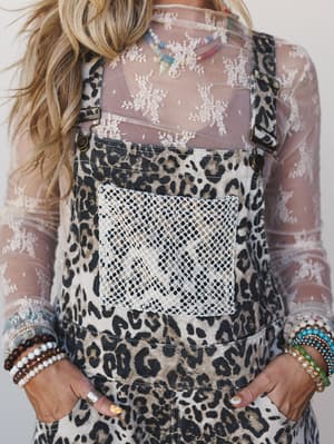 A close-up torso shot of leopard print overalls layered over a sheer floral lace top, styled with stacked beaded bracelets and layered necklaces — the kind of outfit that looks effortless but clearly wasn't an accident.